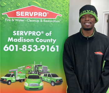 Male employee in a black jacket standing in front of a SERVPRO banner